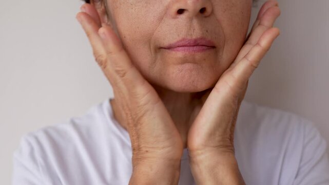 Close-up of a mature woman massaging her lower face and neck, pinching and smoothing the skin. Visible signs of aging, skincare routine, self-care and natural beauty