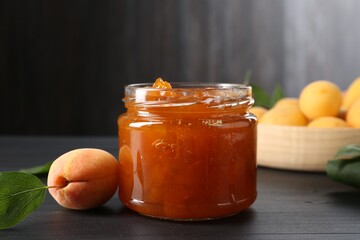 Tasty apricot jam and fresh fruits on black wooden table, closeup