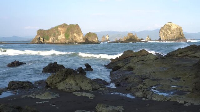 Love Bay - Teluk Love in Jember east java. A scenic view of a rocky cliff surrounded by ocean waves crashing under a blue sky. The intricate rock formations and the dynamic movement of the waves