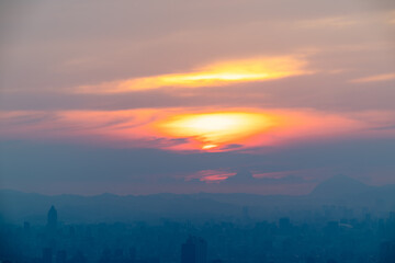 The setting sun peeks through the clouds over Pinglin, New Taipei City, Taiwan, casting soft hues of pink and orange across the sky during twilight.