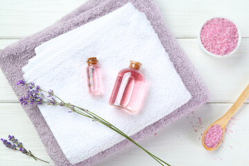Lavender essential oil, flowers, towels and sea salt on white wooden table, flat lay