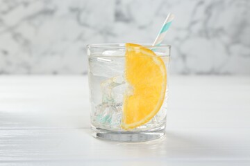 Sparkling water with orange slice in glass on white wooden table, closeup