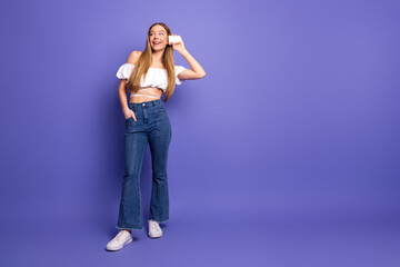 Charming young woman posing stylishly on a purple background with a phone, showcasing casual summer...