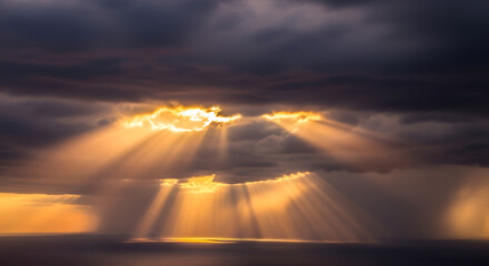 Dramatic Sky with Golden Sunbeams Breaking Through Dark Clouds Over Water.