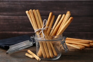 Delicious grissini sticks in open glass jar on wooden table, closeup