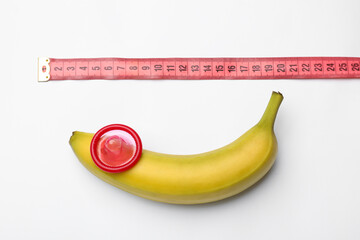 Sex education. Banana with condom and measuring tape on white background, top view