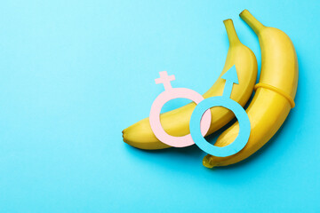 Sex education. Bananas with condom, paper female and male gender symbols on light blue background,...