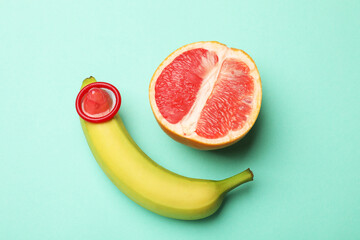 Sex education. Banana with condom and grapefruit on turquoise background, top view