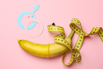 Sex education. Banana with condom, measuring tape, paper female and male gender symbols on pink...