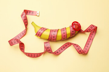 Sex education. Banana with condom and measuring tape on beige background, top view