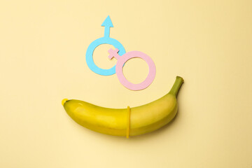 Sex education. Banana with condom, paper female and male gender symbols on beige background, flat...