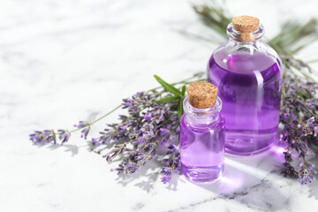 Aromatic essential oil in bottles and lavender flowers on white marble table, closeup