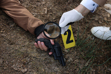 Forensic expertise. Detective with magnifying glass working at crime scene with dead man's body...