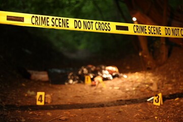 Forensic expertise. Crime scene with dead man's body and markers outdoors, focus on police tape