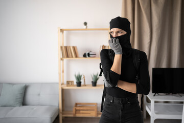 Burglar, robber and thief. Thoughtful young woman wearing black balaclava and gloves into...