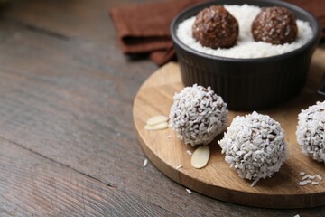 Delicious homemade candies with coconut flakes on wooden table, closeup. Space for text