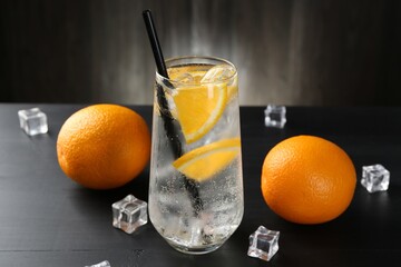 Refreshing soda water with orange slices and ice cubes on black wooden table, closeup