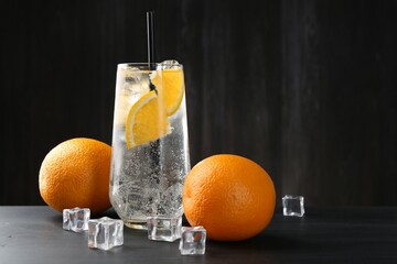 Refreshing soda water with orange slices and ice cubes on black wooden table. Space for text