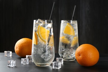 Refreshing soda water with orange slices and ice cubes on black wooden table, closeup