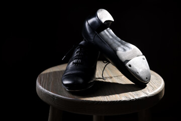 Pair of shoes for tap dance on wooden stool against black background, closeup