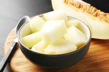 Cut ripe melon in bowl on black wooden table, closeup