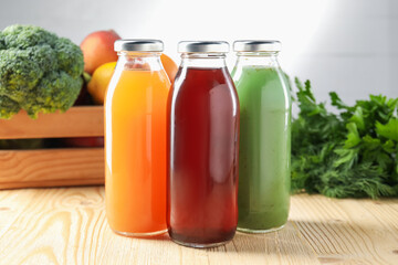 Tasty juices in glass bottles, fresh ingredients and herbs on wooden table against light grey...