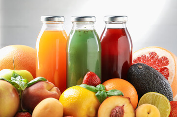 Tasty juices in glass bottles, fresh ingredients and basil against light grey background, closeup