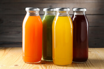 Tasty juices in glass bottles on wooden table against brown background, closeup