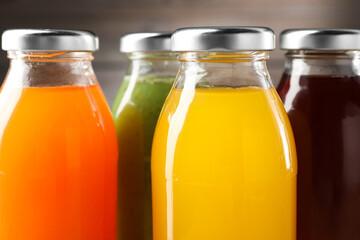 Tasty juices in glass bottles against blurred brown background, closeup