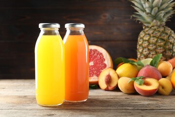 Tasty juices in glass bottles, fresh ingredients and herbs on wooden table against brown background, closeup