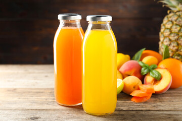 Tasty juices in glass bottles, fresh ingredients and herbs on wooden table against brown...