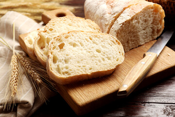 Fresh bread, knife and wheat spikes on wooden table, closeup
