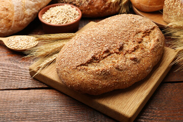 Loaves of fresh bread, grains and wheat spikes on wooden table, closeup