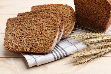 Pieces of fresh bread and wheat spikes on wooden table, closeup