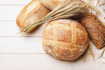 Different types of bread and wheat spikes on wooden table, flat lay. Space for text