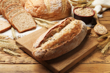 Different types of bread, grains and wheat spikes on wooden table, closeup