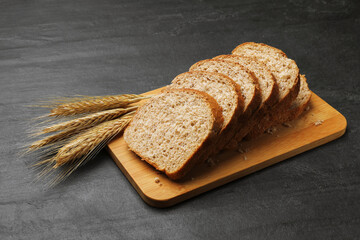 Pieces of fresh bread and wheat spikes on black table, closeup