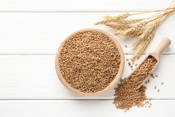 Wheat grains in bowl, scoop and spikelets on white wooden table, flat lay. Space for text