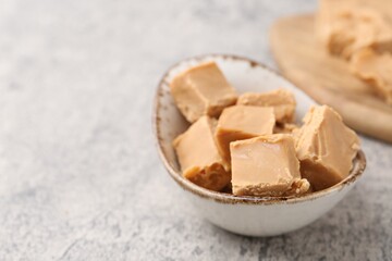 Homemade caramel candies in bowl on light grey table, closeup. Space for text