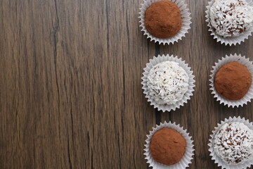 Delicious homemade candies with cocoa powder and coconut flakes on wooden table, flat lay. Space...