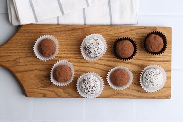 Delicious homemade candies with cocoa powder and coconut flakes on white table, top view