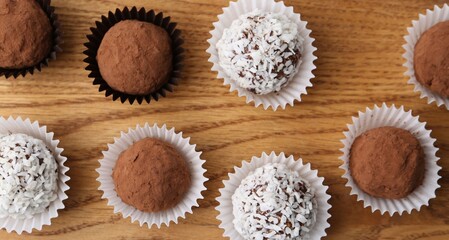 Delicious homemade candies with cocoa powder and coconut flakes on wooden table, flat lay
