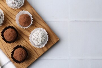 Delicious homemade candies with cocoa powder and coconut flakes on white tiled table, top view....