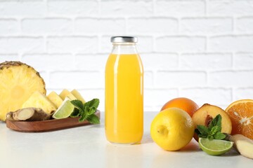 Tasty juice in glass bottle, fresh fruits, ginger and mint on white table against brick wall