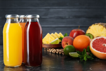 Tasty juices in glass bottles, fresh fruits and mint on black marble table, closeup