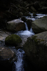 Flowing water among rocks in a dimly lit forest stream