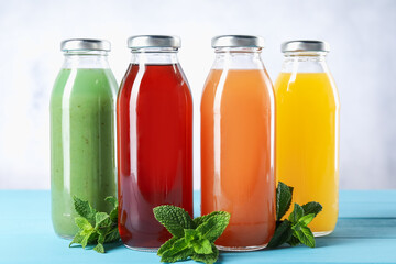 Tasty juices in glass bottles and mint on light blue wooden table, closeup