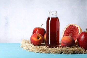 Tasty juice in glass bottle and fresh fruits on light blue wooden table, space for text