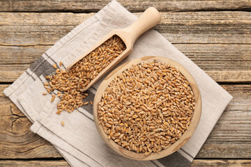 Wheat grains in bowl and scoop on wooden table, flat lay