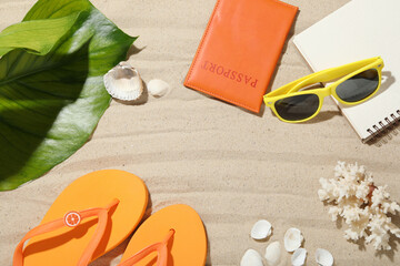 Time for summer vacation. Passport, notebook, green leaf and beach accessories on sand, flat lay. Space for text